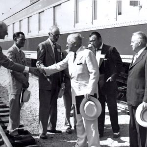 Group of white men in suits standing by a train while two of them shake hands
