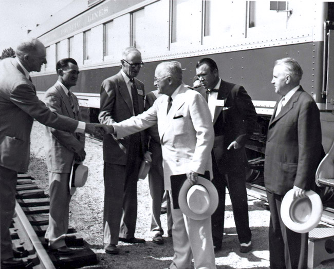 Group of white men in suits standing by a train while two of them shake hands