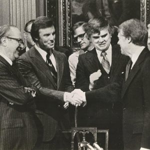 Group of white men in suits shaking hands with white man in suit