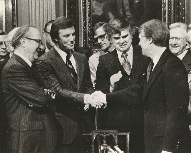 Group of white men in suits shaking hands with white man in suit