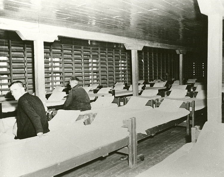 Two white men sitting on beds in barracks building