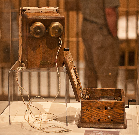 Telephone bells and open wooden box with crank handle in glass display case
