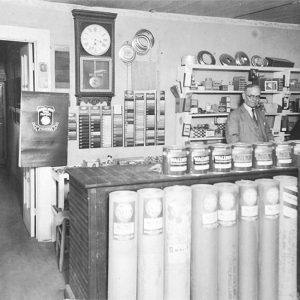 Two white people standing behind counter in store displaying various goods