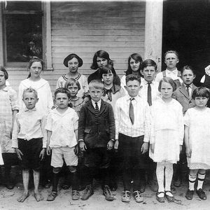 Young white woman with white students and school house