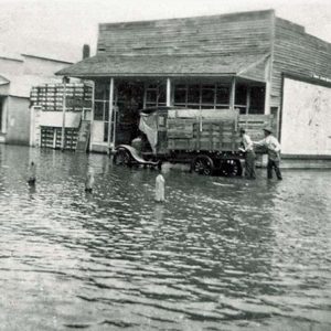 Truck stuck on flooded street with men in hats and store fronts