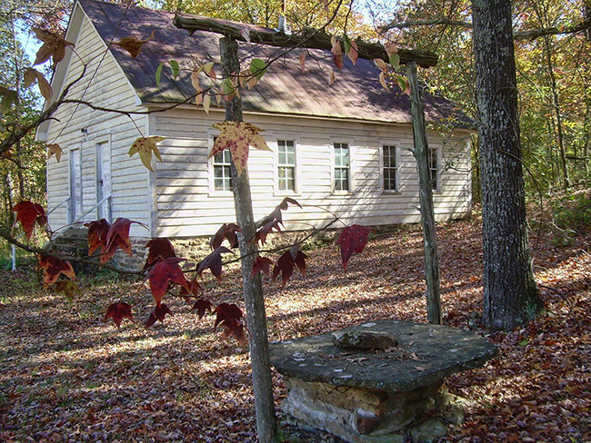 Side-view of single-story school house with wood siding and well in the foreground