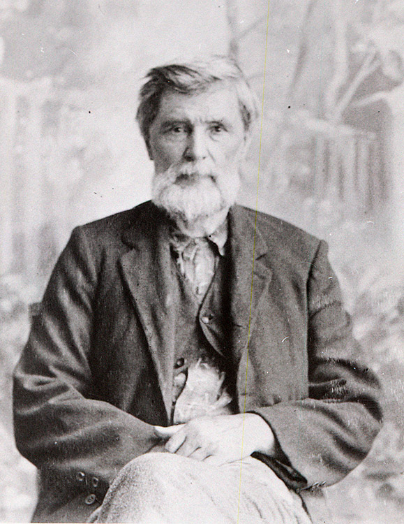 White man with beard sitting in suit with hands in his lap