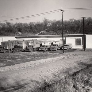 Fleet of trucks parked outside warehouse building on dirt road