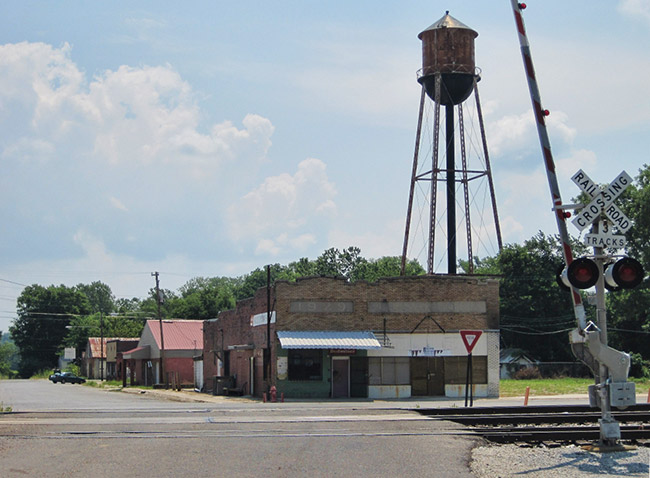 Street with railroad crossing and brick buildings with water tower