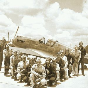 Group of African-American men in military uniforms posing in formation on airstrip with airplane and buildings behind them