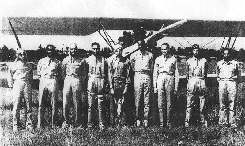 Group of African-American men standing in line with biplane behind them