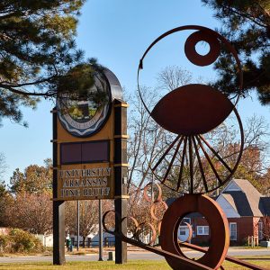"University Arkansas Pine Bluff" sign with seal on grass and abstract sculpture in the foreground