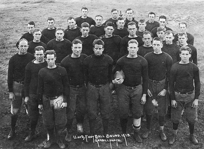Group of young white men in matching dark colored uniforms standing together on field