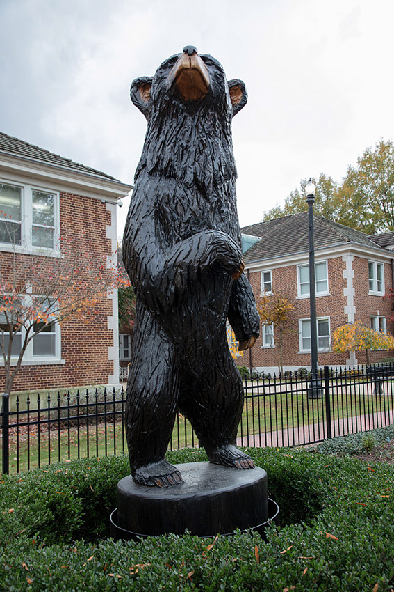Close-up of bear statue on pedestal with multistory brick buildings behind it inside iron fence
