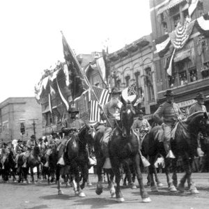 White men in Confederate uniforms and hats holding Confederate flags ride on horseback in a parade