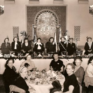 Group of older white women in formal clothing posing at tables in dining hall