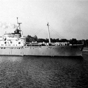 Side view of long ship underway with shore in the background