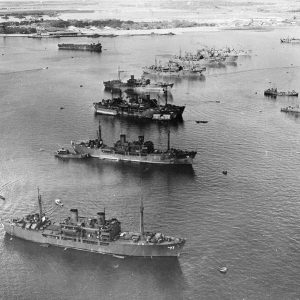 Row of Naval vessels in bay with shore in the background