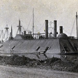 Ironclad boat tied to the shore with sailors on board and other boats in background