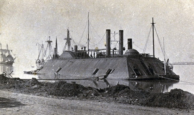 Ironclad boat tied to the shore with sailors on board and other boats in background