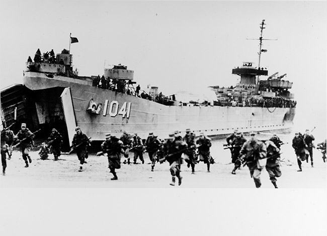 Soldiers with guns running from beached Naval vessel with bow doors open and sailors watching from its deck
