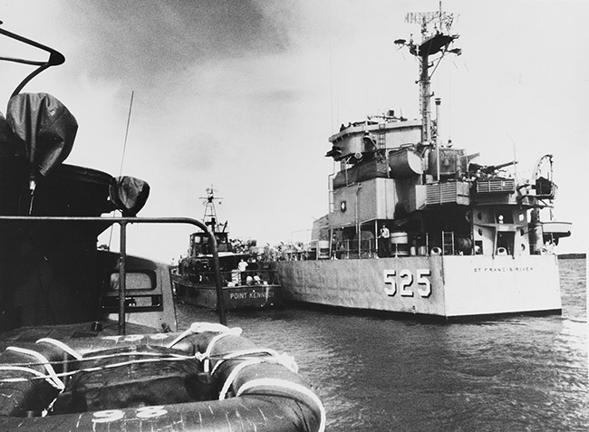 View from small boat of another small boat guiding Naval vessel with "525" on its stern