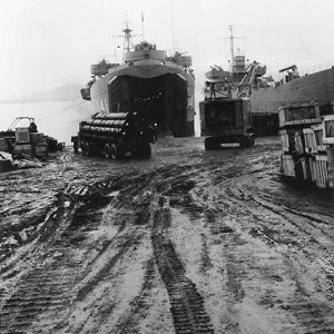 Two Naval vessels being unloaded by trucks on muddy shore