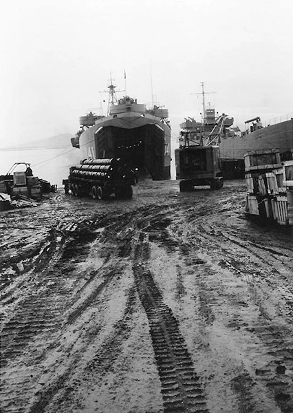 Two Naval vessels being unloaded by trucks on muddy shore