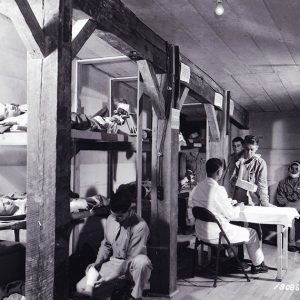 White men in uniform with doctor at desk and men lying in bunk beds in underground room