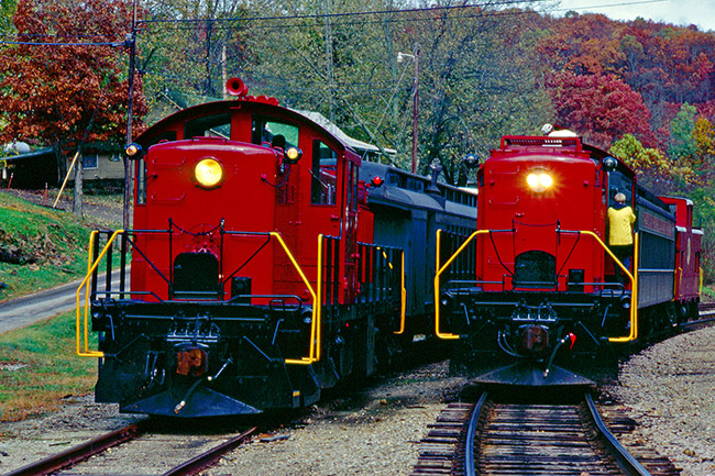 Pair of red trains with cars passing each other on tracks