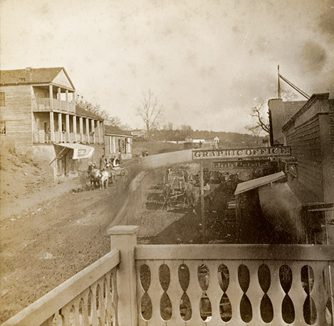 View from balcony looking out at horse drawn wagon on dirt road with multistory buildings on both sides