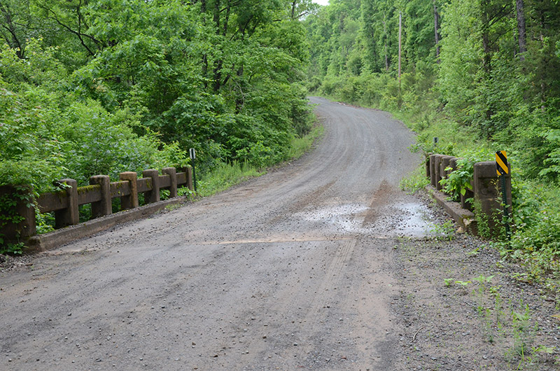 Gravel road over concrete bridge with trees on both sides