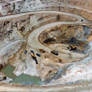 Aerial view of excavator and other vehicles at the end of a winding dirt road leading to the bottom of an open pit mine