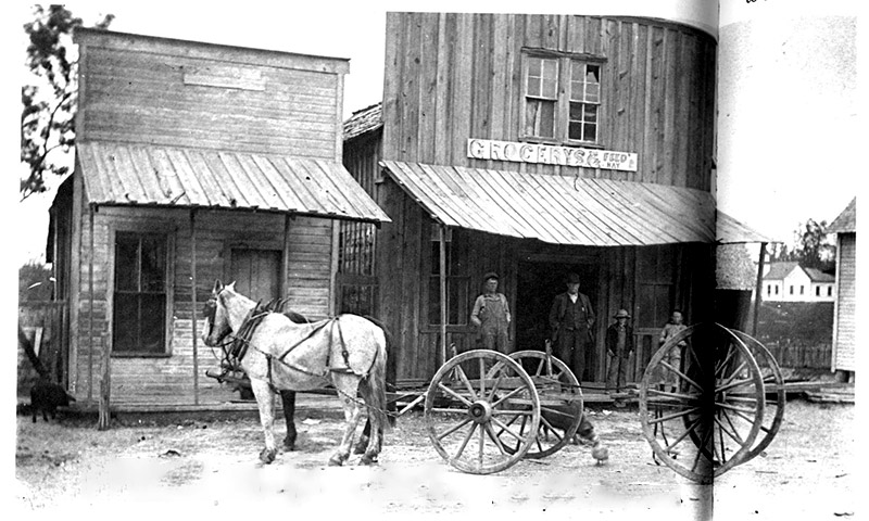 People standing on porch or wooden storefront behind horse and buggy