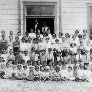Large group of adults and children posing in front of wooden building