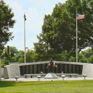 Memorial wall with plaque long stone bench and statue with flags and flowers