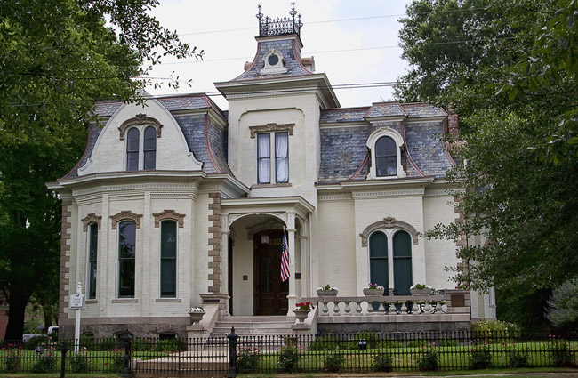 Elaborate multistory manor house with arched windows and iron fence