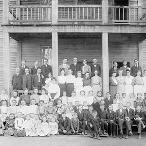 Group of white students and faculty at two-story school building