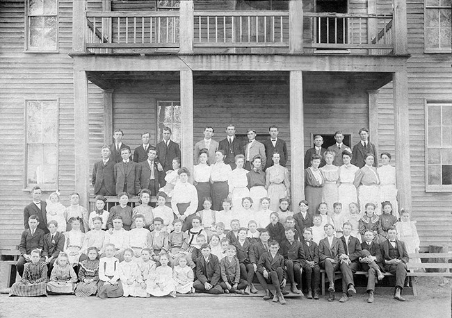Group of white students and faculty at two-story school building