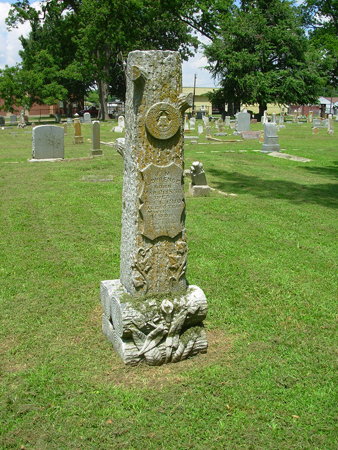 Log shaped monument in cemetery with Woodsmen of the World symbol and engraved shield on it