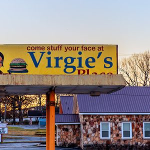 Side view of single-story building with rock walls under "Virgie's Place" billboard