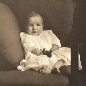 White baby boy with toy leaning against cushions