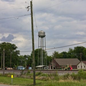 Brick building and playground equipment near water tower with road and railroad tracks in the foreground