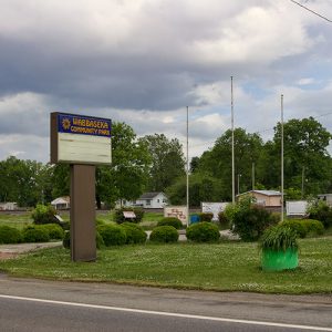 "Wabbaseka Community Park" sign and flag poles on street with single-story buildings and houses in the background