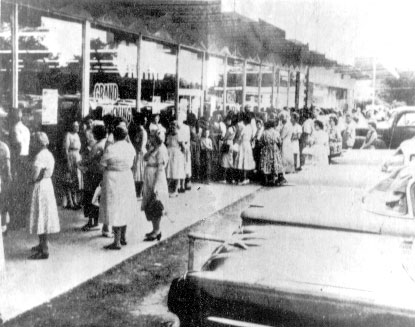 Crowd waiting outside a supermarket with parked cars