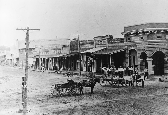 Dirt road with buildings and horse drawn wagons