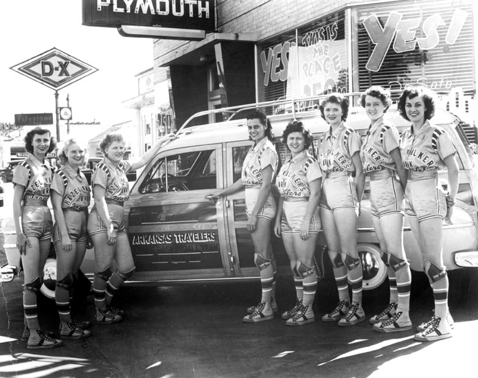 White women in uniforms posing with "Arkansas Travelers" station wagon in front of building with "Plymouth" sign