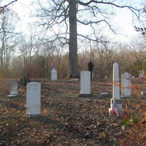 White gravestones and obelisk marker in cemetery under autumn trees