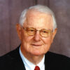 Old white man with glasses smiling in suit and tie