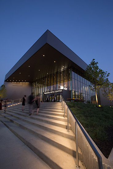 "Walton Arts Center" building with concrete steps glass covered entrance and flat roof shown at twilight with lights inside